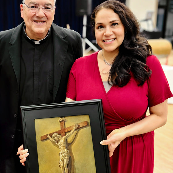 Priest and Artist Maria Rangel Cardenas holding a framed artwork of the crucifixion.